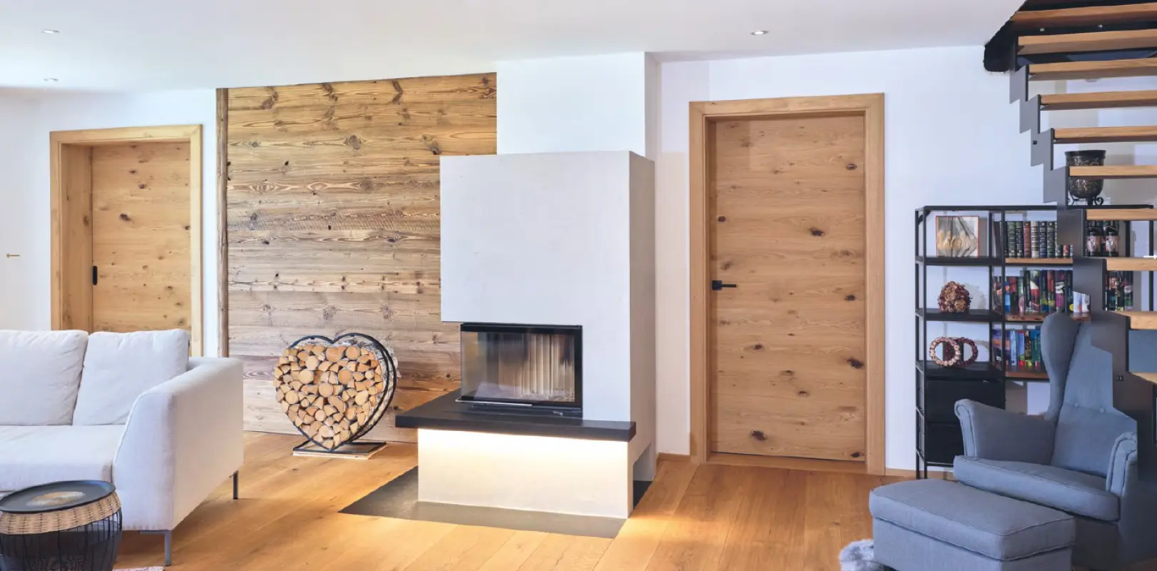 modernes helles Wohnzimmer mit Kamin, Innentüren aus Holz, Sessel, Sofa, Brennholz